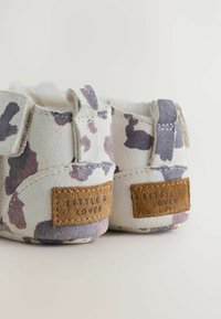 Stivaletti in camoscio bianco con motivo a macchie viola e grigie, dotati di rivestimento morbido, strap in velcro e un'etichetta marrone sul retro.