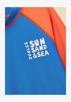Modro-oranžna majica z dolgimi rokavi s belim napisom "Joules Sun Sand & Sea" na sprednji strani.