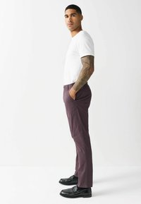 Herren-fitted weißes T-Shirt, kombiniert mit dunkelmaulwurf farbenen Hosen. Die Hosen verfügen über Seitentaschen und ein schlankes Design. Getragen mit schwarzen Lederschuhen.