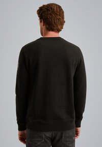Sudadera negra de manga larga con puños acanalados, presenta un escote redondo y una textura suave. La vista posterior muestra un diseño minimalista.