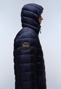 Chaqueta de plumas azul marino con capucha, con diseño acolchado, un parche naranja en la manga y detalle de cremallera azul en contraste.
