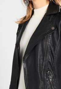 Černá kožená motocyklová bunda s klopovým límcem, zapínáním na zip a bočními kapsami. Texturovaný povrch s kovovými prvky v stříbrné barvě.