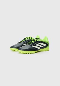 Bottines de football noires et vert fluo avec une tige synthétique texturée, maintenues par des lacets noirs, avec des rayures blanches et une semelle en caoutchouc avec des crampons.
