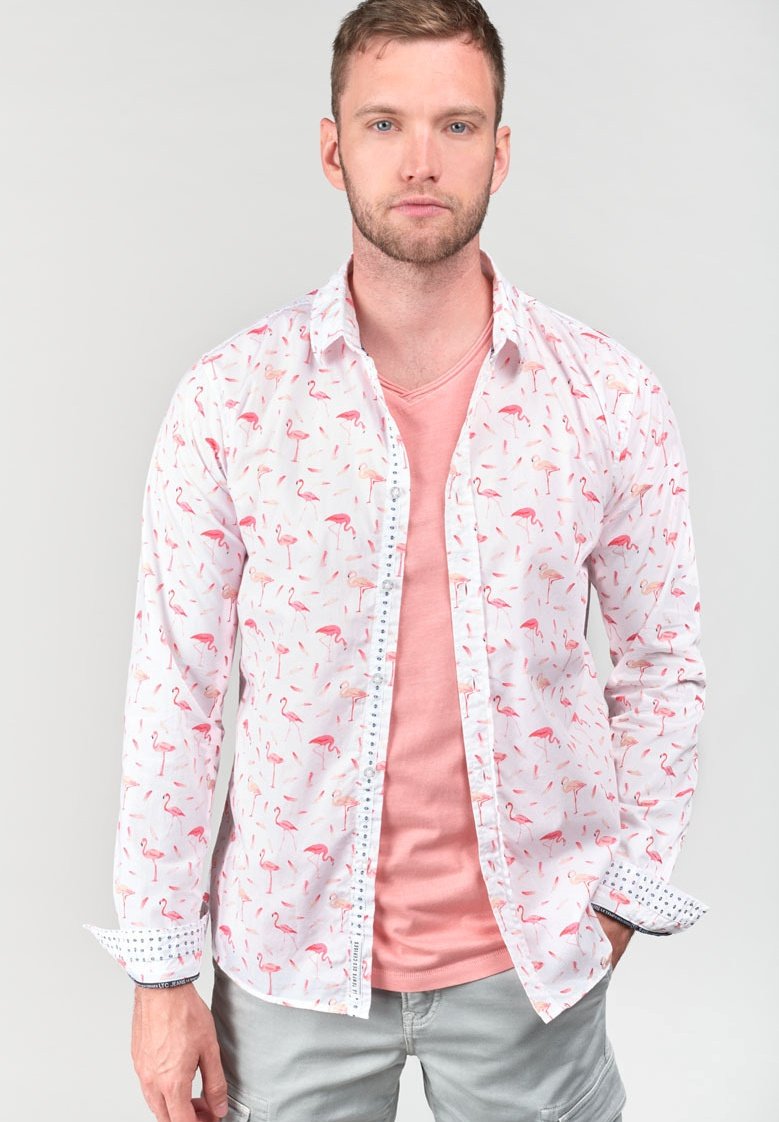 Witte shirt met een roze flamingo-print, knoopsluiting aan de voorkant, gecombineerd met een roze V-hals t-shirt. Grijze shorts met patroon aan de manchetten.