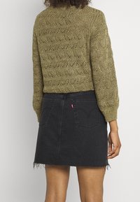 Suéter de color verde oliva de punto con textura ondulada, combinado con una falda de mezclilla negra en corte A que presenta un dobladillo deshilachado y bolsillos traseros.