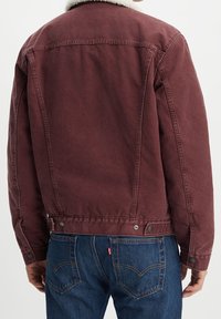 Burgundy denimjacka med en vit pälskrage, som har rak skärning, metallknappar och detaljer i bakseam.