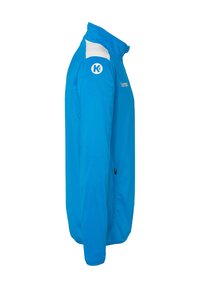 Blå sportjakke med høj krave, hvid skulderaccent og logo. Har en lynlåslomme på siden og en glat stofoverflade.