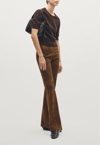 Brown suede flared pants paired with a dark brown short-sleeve sweater; model holds a small black handbag. Smooth textures, simple design.