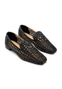 Mocasines trenzados negros con un diseño de malla abierta, punta afilada y suela plana. Presentan un interior de cuero y acentos marrones en contraste.