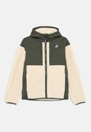 Veste à capuche avec un dessus en nylon vert foncé et un bas en polaire crème, équipée d'une fermeture éclair à l'avant et d'un patch logo sur la poitrine.