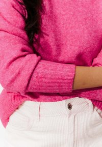 Pull fuchsia en rose avec un poignet côtelé, fabriqué à partir d'un matériau doux, associé à un pantalon en velours côtelé rose clair avec un détail de bouton.