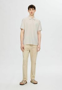 Světlebarevné polo tričko s polosou zipem, kombinované s béžovými kalhotami a hnědými nazouvacími sandály. Jednoduchý design s krátkým rukávem a volným střihem.
