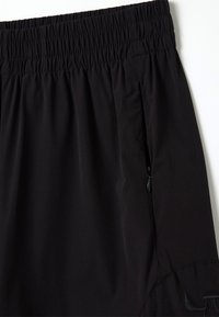Shorts noirs en tissu léger avec une taille élastique. Comprend une poche latérale zippée et des détails cousus.