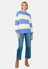 Sinine ja valge triibuline kootud kampsun, ribatekstuuri ja ümmarguse kaelusega, koos helesiniste sirgete pükste ja pruunide kontsakingadega.