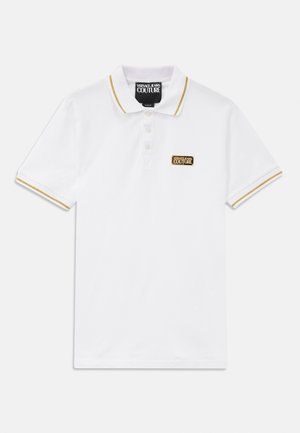 Hvit polo-skjorte med gull-stripete krage og ermer. Har et lite svart og gull-logo-patch på brystet. Laget av bomull.