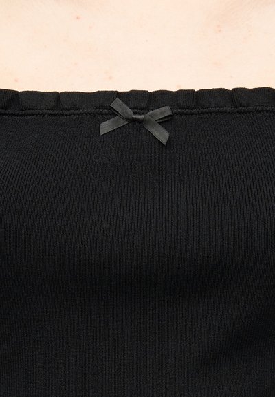 Μαύρο ριγωτό ύφασμα με ένα μικρό διακοσμητικό μαύρο φιόγκο στο κέντρο κατά μήκος της πάνω άκρης, πάνω σε ανοιχτόχρωμο δέρμα.