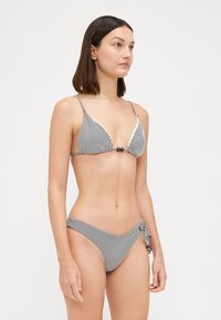 Costume da bagno a righe bianche e nere composto da un top triangolare e un pantaloncino con allacciatura laterale regolabile e dettagli hardware decorativi.