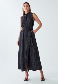 Czarna, bezrękawnikowa sukienka maxi w białe kropki, z guzikami z przodu, wiązanym w pasie i tiered hem. Gładki materiał, luźny krój, boczne kieszenie.