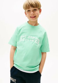 T-shirt in cotone verde menta con maniche corte, caratterizzata dal logo bianco "Hilfiger". Design aderente con scollo rotondo e maniche raglan.