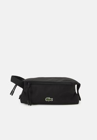 Neceser negro hecho de tela duradera, con forma rectangular, cierre de cremallera y un pequeño logo de cocodrilo bordado en verde.