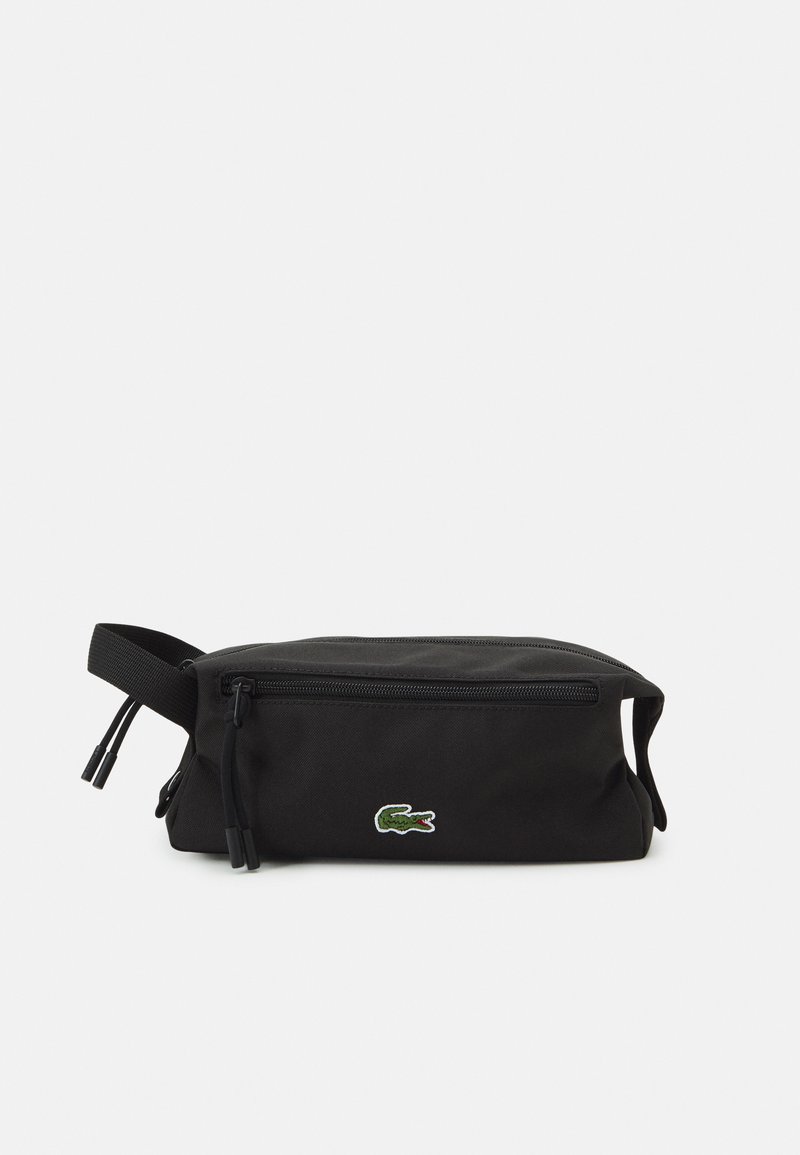 Neceser negro hecho de tela duradera, con forma rectangular, cierre de cremallera y un pequeño logo de cocodrilo bordado en verde.