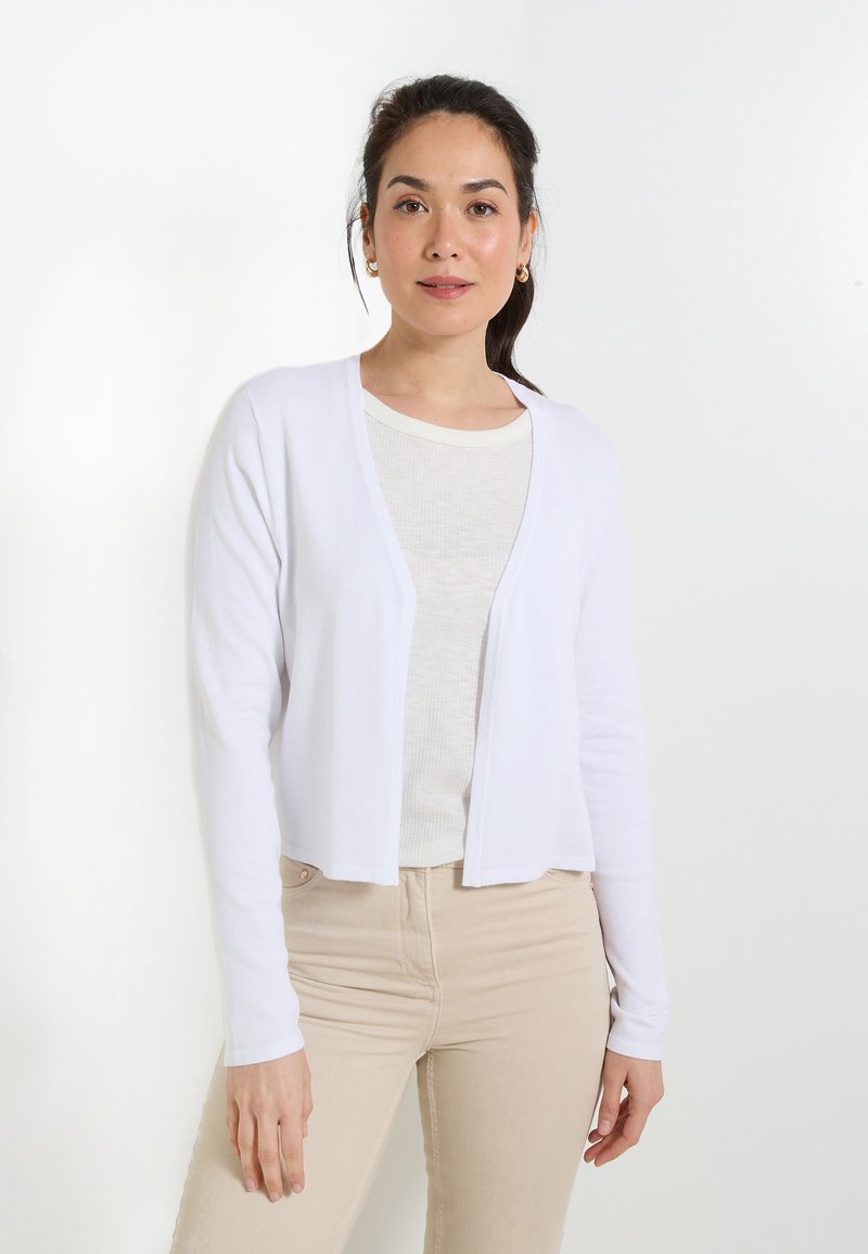 Cárdigan blanco con un diseño corto, hecho de una tela suave, con mangas largas y un frente abierto, llevado sobre una blusa ligera y texturizada.