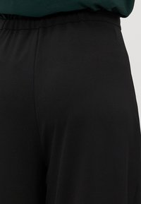 Zwarte broek met een elastische tailleband, met een gladde textuur en een wijd beenontwerp. De stof lijkt lichtgewicht en ademend te zijn.