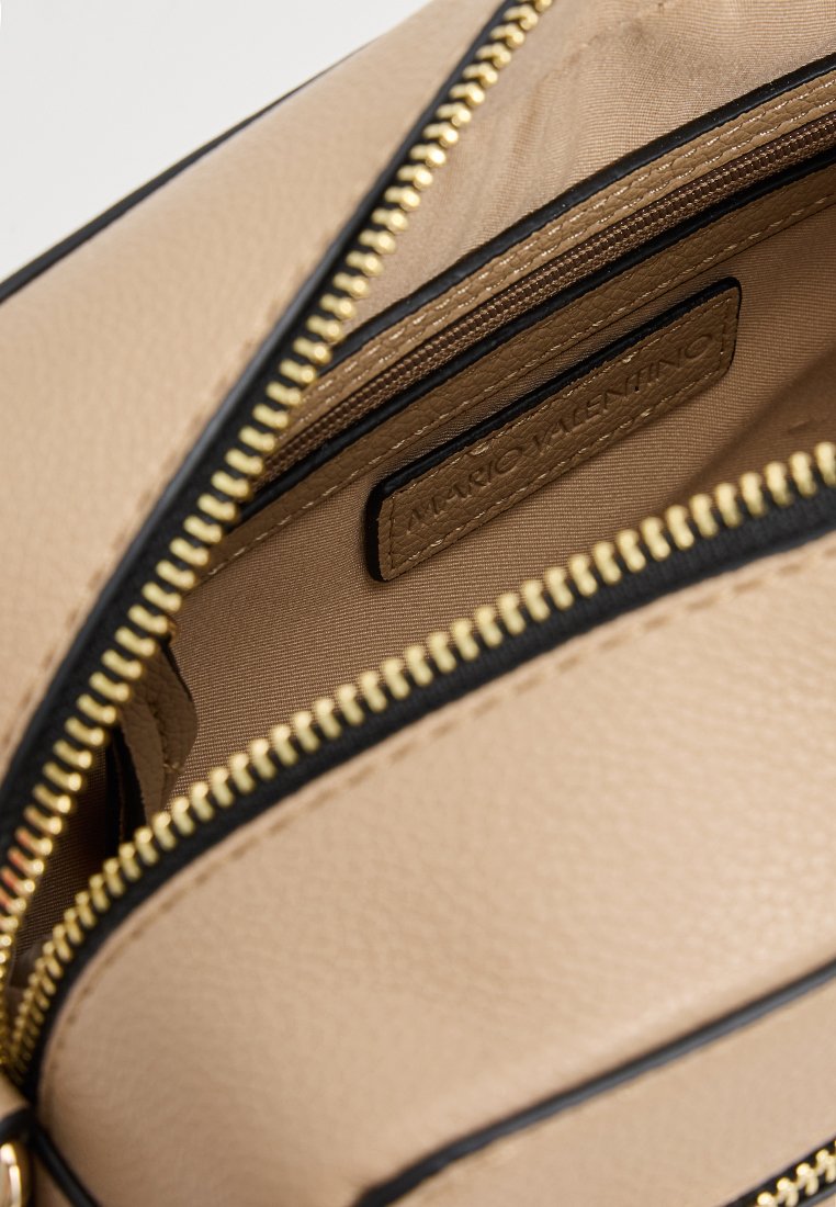 Beige Handtasche mit schwarzen Akzenten, ausgestattet mit goldenen Reißverschlüssen und einem strukturierten Design. Enthält ein Etikett im Inneren der Tasche.