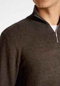 Maglione marrone con zip realizzato in tessuto morbido e testurizzato. Presenta un colletto alto e una zip metallica, con un design aderente.