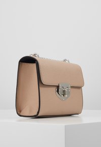 Beżowa syntetyczna torebka o fakturowanej powierzchni, srebrnych elementach i zamknięciu na klapę. Posiada czarny obrys i pasek łańcuchowy.