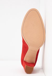 Chaussure à talon haut en daim rouge avec une semelle en caoutchouc texturée, présentant un bout arrondi lisse et une silhouette élégante. Nom de la marque "Clarkson" embossé.