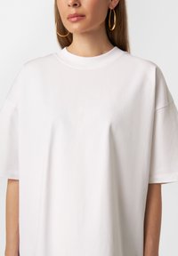 Hvid oversized bomulds-t-shirt med rund halsudskæring, korte ærmer og en glat tekstur. Har subtile sømdetaljer.