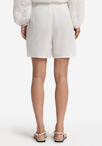 Vita linnebyxor med en avslappnad passform, som har ett slätt, strukturerat tyg och en enkel fåll. Bärs tillsammans med ljusa sandaler.