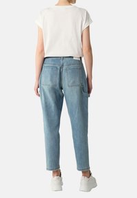 Lichtblauwe denim jeans met een relaxte pasvorm, twee achterzakken en een zijzak, gecombineerd met een wit T-shirt met korte mouwen en sneakers.