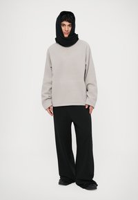 Sweatshirt cinza de fleece com um bolso, combinado com calças largas pretas. Um cachecol preto cobre a cabeça, criando um visual em camadas. Textura suave por toda a peça.