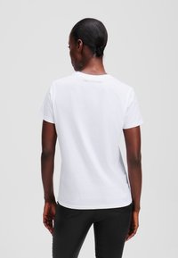 Weißes Baumwoll-T-Shirt mit rundem Halsausschnitt und kurzen Ärmeln, das eine glatte Textur und ein einfaches Design aufweist, von hinten betrachtet.