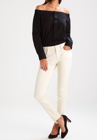 Svart blus med off-shoulder och knappar framtill, kombinerad med figurnära cremefärgade byxor och svarta klackar med sköldpaddsmönstrad detalj.