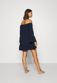 Vestido navy de un solo hombro con mangas acampanadas, dobladillo con volantes y detalles bordados, confeccionado con una tela suave y un corte holgado.