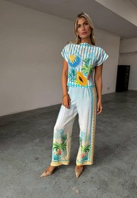 Ensemble deux pièces comprenant un haut à manches courtes avec des imprimés de fruits tropicaux bleus et jaunes, assorti à un pantalon large en couleurs claires avec des accents de palmiers.
