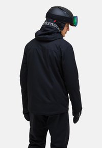 Schwarze Skijacke aus wasserabweisendem Material, mit Kapuze, kontrastierendem Logo auf dem Rücken und passenden Handschuhen.