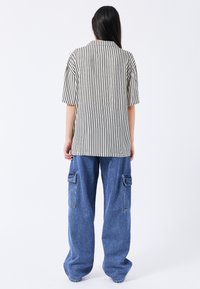 Gestreiftes kurzärmeliges Hemd in Creme und Schwarz, kombiniert mit lockeren blauen Denim-Cargohosen mit großen Seitentaschen.