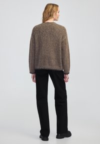 Bruine, fuzzy gebreide trui met een relaxte pasvorm, ronde halslijn en zwarte afwerking langs de zoom. Gecombineerd met zwarte recht gesneden broek.