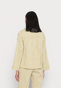 Blusa de padrão xadrez verde e branco com um corte descontraído, mangas longas e um detalhe na parte de trás com botões. Combinada com calças a condizer.