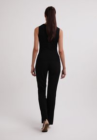 Top senza maniche nero abbinato a pantaloni neri slim-fit. Le scarpe sono beige con tacco basso. Tessuto morbido, silhouette aderente e design minimal.