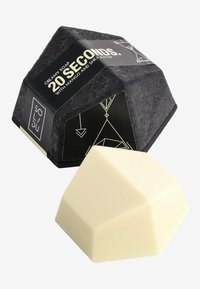 Creamy soap in a geometric white shape beside a black hexagonal packaging with gold text and geometric design elements.