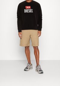 Felpa nera con logo "DIESEL", pantaloni corti khaki e sneakers grigi con accenti viola. Focus sull'abbigliamento informale per il clima caldo.