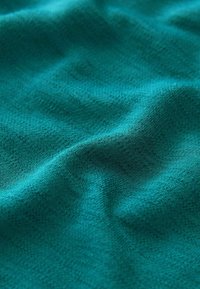 Gros plan d’un tissu bleu sarcelle avec une texture douce et fine et des plis délicats créant des ombres subtiles et de la profondeur.