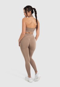 Tan cropped top en bijpassende hoge taille legging van rekbare stof. Witte logo-accenten en gladde textuur. Witte sneakers met een geplaatste zool.