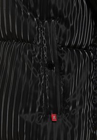 Czarna kurtka puchowa z błyszczącego, teksturowanego materiału z pionowymi liniami, z zapięciem na guziki oraz małą czerwoną metką z logo.