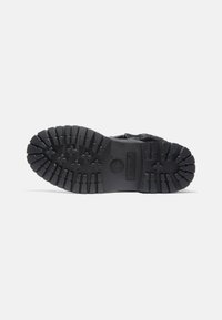 Suela de bota de goma negra con patrón de surcos profundos, con detalles en forma de cruz y círculos elevados, logotipo de la marca en el talón, diseño resistente.